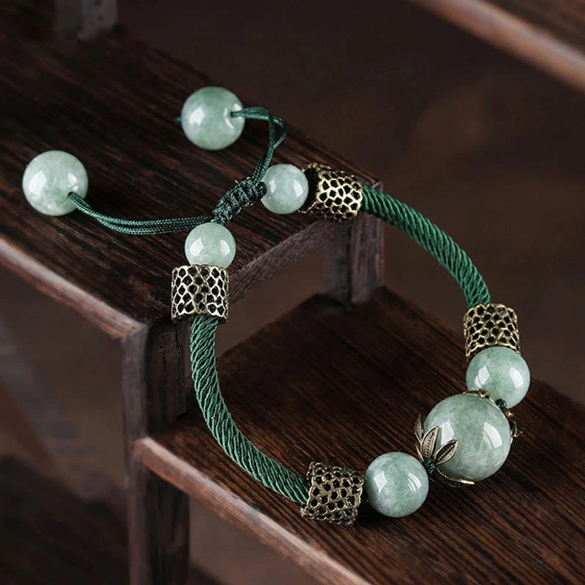 Three-quarter view of green jade prosperity bracelet with extra beads hanging from pull cord and vintage metal hardware