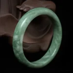 Natural green jade cuff bangle bracelet with marbled design on wooden background