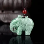 Natural green jade elephant pendant necklace with intricate hand-carved details, traditional brown waxed cord and red glass accent bead, displayed on dark reflective surface