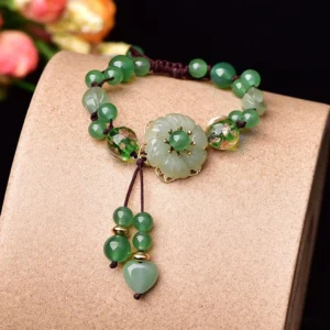 Green jade flower dangle bracelet overhead flat lay on light brown jewelry display with adjustable brown cord