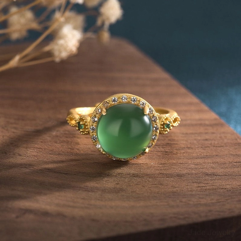 Green jade fortune ring with crystal halo setting front view on wooden table with dried flowers