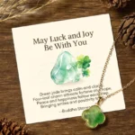 Green jade four-leaf clover luck necklace with personalized blessing message card, gold-plated pendant, and delicate chain displayed on wooden table with natural pinecones