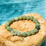 Green jade Fu character bracelet flat lay with gold flower accent and Fu charm on stone background