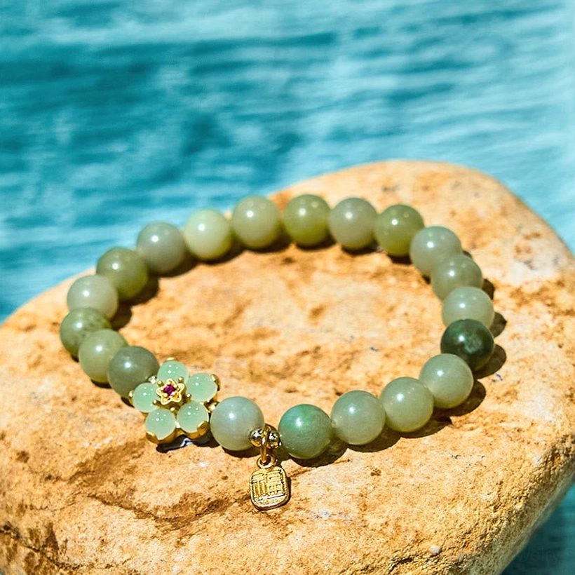 Green jade Fu character bracelet flat lay with gold flower accent and Fu charm on stone background