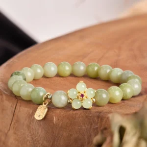 Green jade fu charm bracelet with gold flower pendant displayed on wooden round tray - overhead flat lay view