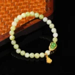 Green jade beaded lucky bracelet with gold Fu character charm and jade gourd pendant on woven wooden coaster