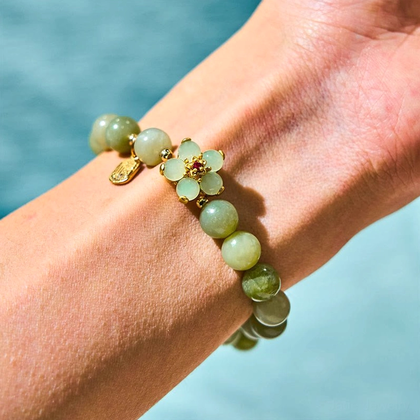 Green jade prosperity bracelet worn on wrist with polished jade beads and gold floral decoration