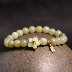 Green jade fortune bracelet overhead view on textured stone surface featuring gradient jade beads, golden floral charm, and metal Fu pendant