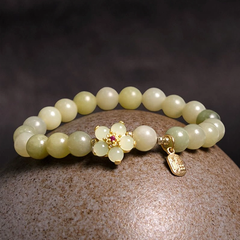 Green jade fortune bracelet overhead view on textured stone surface featuring gradient jade beads, golden floral charm, and metal Fu pendant