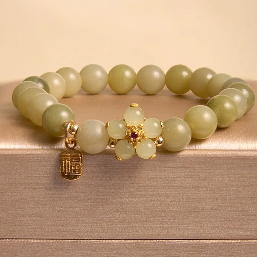 Jade bracelet with pale green round beads and gold flower charm featuring red gemstone accent with Fu pendant on satin gift box
