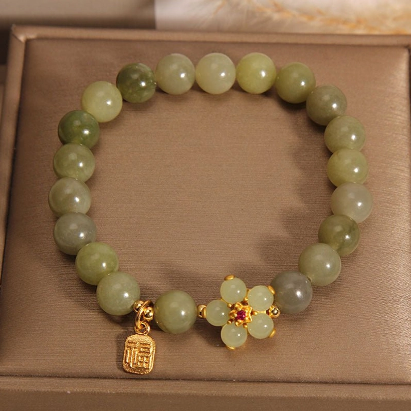 Green jade beaded bracelet displayed inside luxury brown gift box showing light green polished beads with gold flower decoration