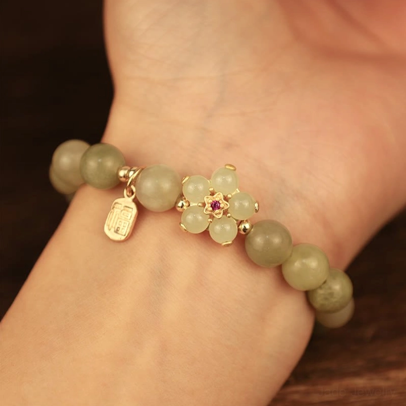 Woman wearing green jade beaded bracelet on wrist showing how the bracelet fits and looks when worn with flower and Fu charm details visible