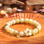 Green jade Fu flower bracelet with gold-toned charm displayed on wooden round tray, showing top-down overhead view of the complete design