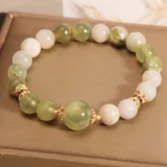 Green and white jade beaded abundance bracelet with gold spacers on brown display tray