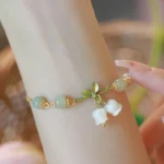 Green jade lily of the valley prosperity bracelet worn on wrist, showing light green jade beads, gold chain, and delicate white lily charms with green leaves