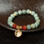 Green jade Om Mani Padme Hum bracelet with rotating gold charm pendant and red engraved mantra beads on dark ceramic plate