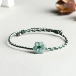 Dark green and light gray braided jade orchid prosperity bracelet with adjustable knot, displayed on minimalist light background