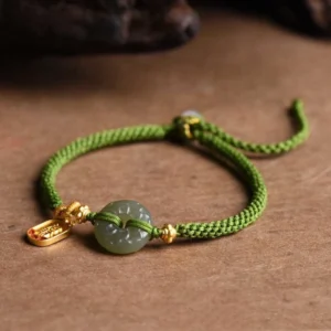 Green jade peace buckle bracelet with gold charm overhead view on wooden surface
