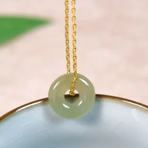 Natural green jade peace buckle necklace with gold twisted chain, close-up side view on ceramic surface