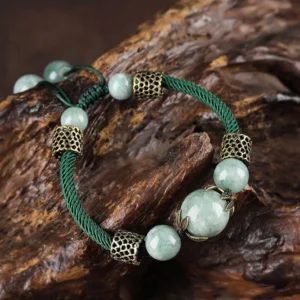 Handmade green jade prosperity bracelet with dark braided rope and antique bronze spacers, displayed on weathered wood