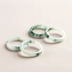 Natural green jade band rings with floating flower patterns displayed in oblique top-down view, showing multiple rings with light base and dark green floral streaks