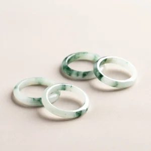 Natural green jade band rings with floating flower patterns displayed in oblique top-down view, showing multiple rings with light base and dark green floral streaks