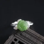 Green jade rose carved into sterling silver leaf-designed adjustable ring, displayed on dark wood surface