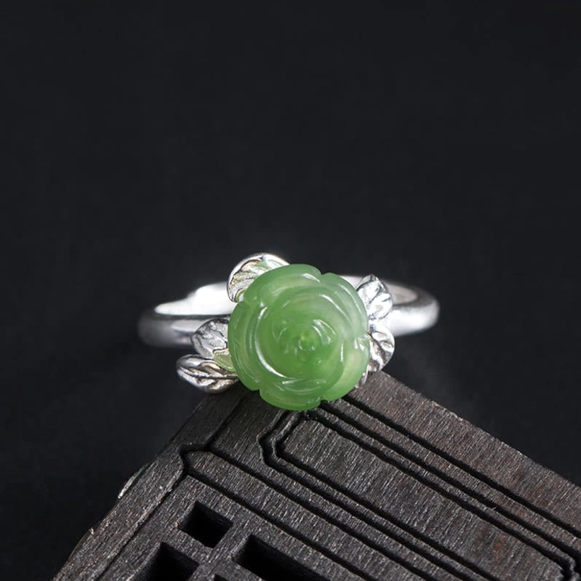 Green jade rose carved into sterling silver leaf-designed adjustable ring, displayed on dark wood surface