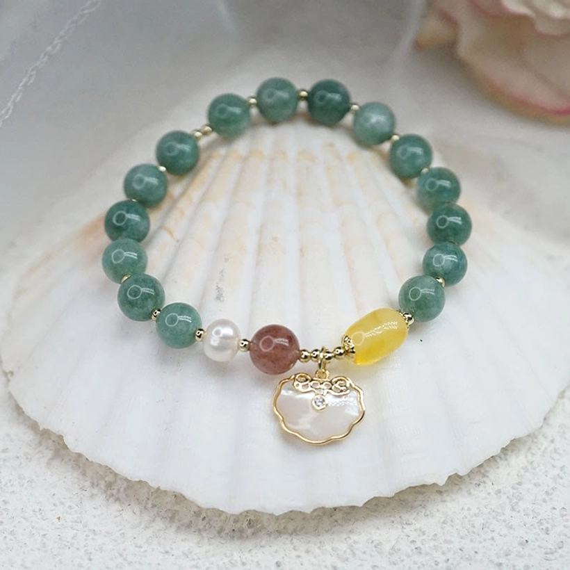 Complete jade Ruyi lock bracelet with sea shell elements displayed on white scallop shell and sand - flat lay composition