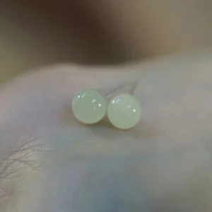 Pale green jade round stud earrings on skin showing translucent beads and silver posts, flat lay