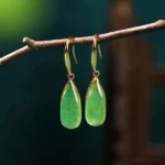 Natural green jade teardrop dangle earrings with vintage gold bezel, hanging on delicate wooden twig, front view showcasing translucent jade stone and French ear wire