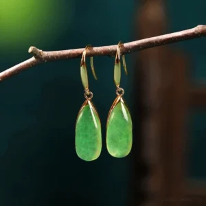Natural green jade teardrop dangle earrings with vintage gold bezel, hanging on delicate wooden twig, front view showcasing translucent jade stone and French ear wire