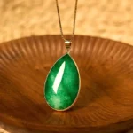 Green jade water drop pendant necklace with gold-plated bezel on wooden background