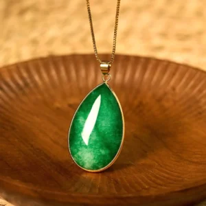 Green jade water drop pendant necklace with gold-plated bezel on wooden background