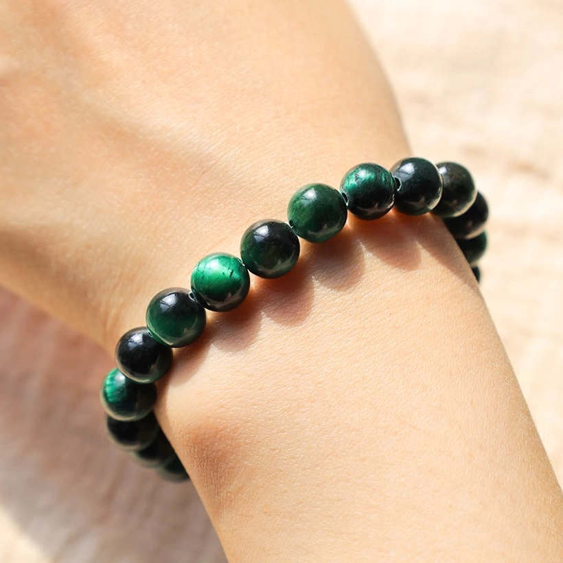 Green tiger eye stone bracelet worn on wrist close-up, indoor setting showing smooth round deep green beads with natural striping