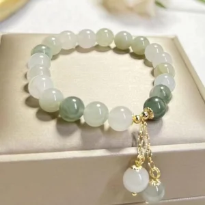 Gradient jade prosperity bracelet flat lay on luxury satin jewelry storage box, showcasing green and white jade beads with elegant gold hardware and dual charm pendants