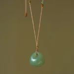 Handcrafted natural jade prosperity pendant necklace with polished light green jade stone on traditional braided tan cord with gold accent beads
