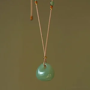 Handcrafted natural jade prosperity pendant necklace with polished light green jade stone on traditional braided tan cord with gold accent beads