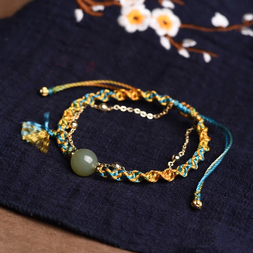 Handmade jade bracelet with blue yellow rope on dark embroidered fabric background