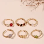 Assorted healing stone adjustable open rings with natural crystal beads in white, red, brown tones on gold alloy bands, flat lay top view