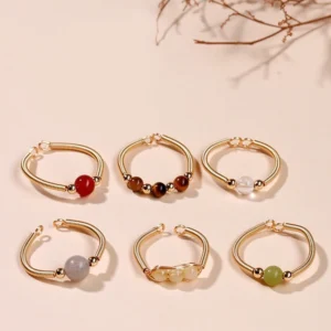Assorted healing stone adjustable open rings with natural crystal beads in white, red, brown tones on gold alloy bands, flat lay top view