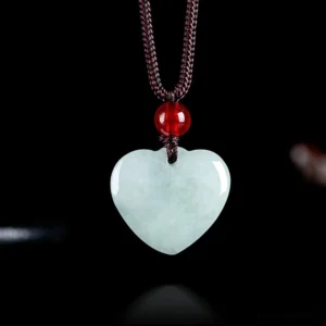 Pale green heart-shaped jade pendant necklace with brown braided cord and red accent bead, frontal view on black background