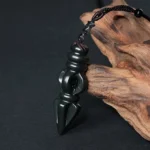 Hetian cyan jade Vajra Dorje pendant necklace with smooth polished surface and intricate ritual dagger carving, displayed on natural driftwood backdrop