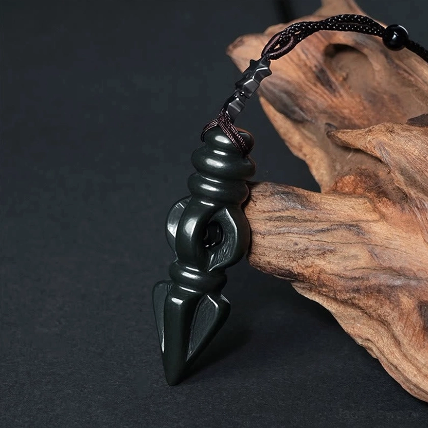 Hetian cyan jade Vajra Dorje pendant necklace with smooth polished surface and intricate ritual dagger carving, displayed on natural driftwood backdrop