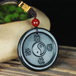 Hetian cyan jade Yin Yang pendant with carved Zhan Yao Zhi Xie characters, front three-quarter view showing red bead and braided cord detail