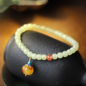Hetian jade beaded bracelet with red agate accent and amber pumpkin charm displayed on black stone background