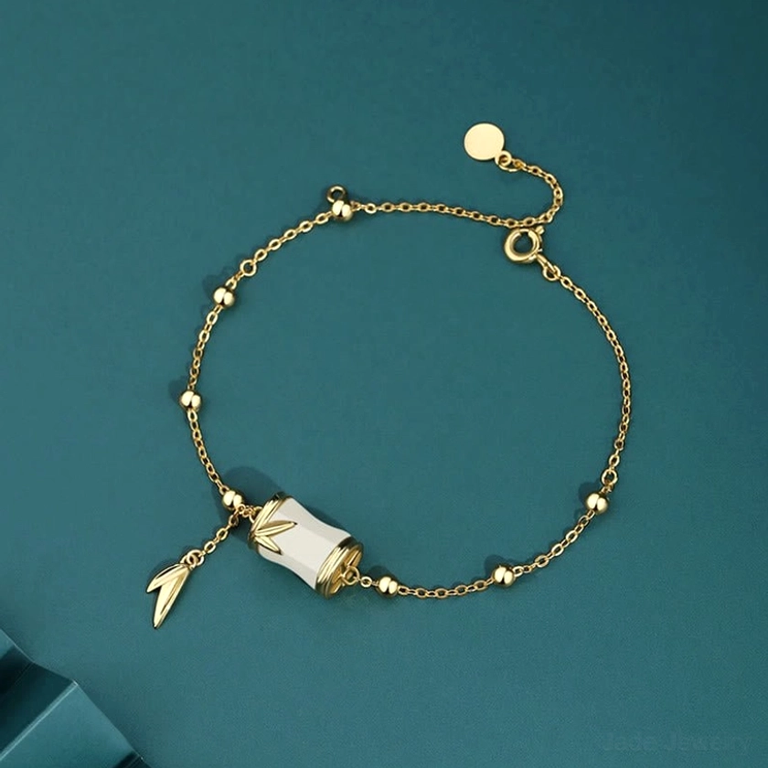 Beaded gold-tone Hetian jade bamboo bracelet featuring white jade bamboo charm, adjustable clasp, and delicate leaf pendant on dark teal studio background