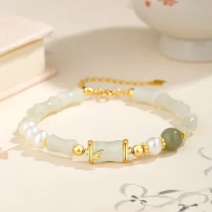 Hetian white jade bamboo charm bracelet with 925 sterling silver on Chinese porcelain tabletop, overhead luxury lifestyle shot