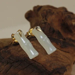Close-up side view of polished hetian jade bamboo stud earring on wooden stand, showing translucent jade and gold-accented silver post