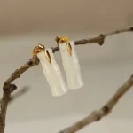 Hetian jade bamboo leaf stud earrings polished finish displayed on natural tree twigs, milky white jade with sterling silver posts